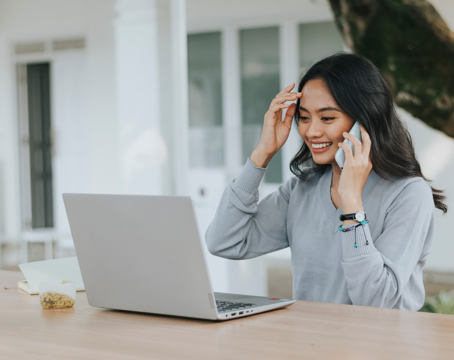 Smiling Woman Calling on Smartphone While Using a Laptop Outdoors